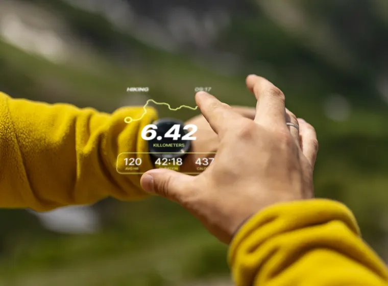 Close-up view of a person using augmented reality technology outdoors, displaying hiking statistics. The background features a blurred natural setting, emphasising innovation and adventure in an outdoor environment.